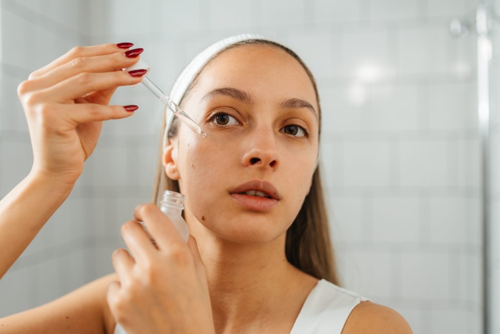 Fiatal nő arcszérumot ken az arcára a fürdőszobában