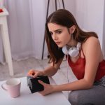 Piros pólós fiatalé lány fülessel a nyakán, pénztárcát tart a kezében és aggódik