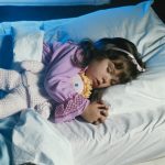 Kislány alszik az ágyában plüssbabával a karjában