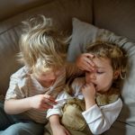 Egy kisgyerek egy másik lázát ellenőrzi tenyerével és lázmérővel