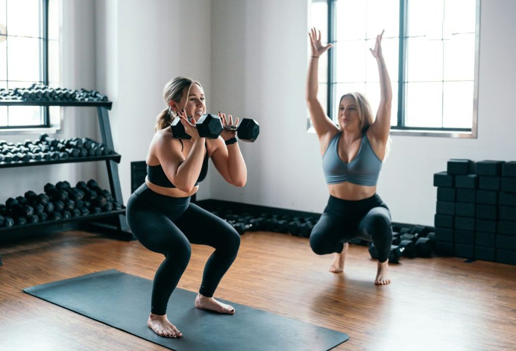 Nő személyi edző mutatja, hogyan végezze a bal oldali nő súllyal a kezében a guggolást vállból nyomással