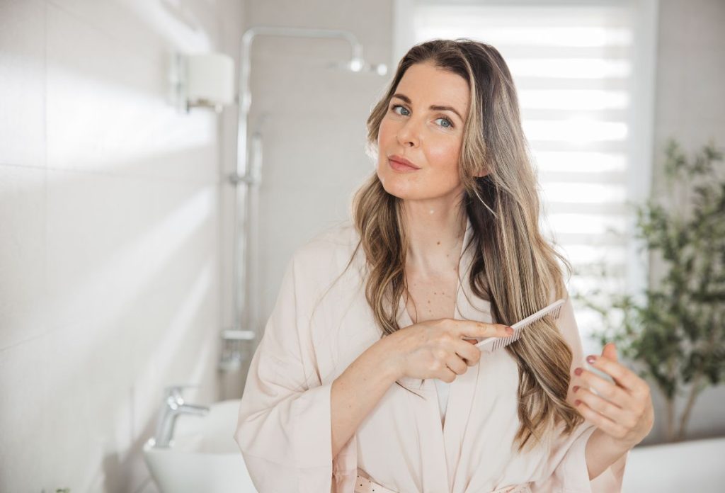 Szép harmincas nő köntösben fésüli a haját és figyeli, mennyire hosszú