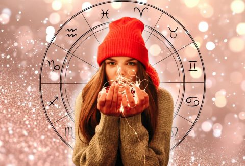 Egy piros sapkás nő barna hajjal, karácsonyi égőket fog, mögötte horoszkóp szimbólum és csillogós háttér