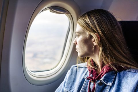Egy nő a repülőgépen ülve komoly arccal néz ki az ablakon