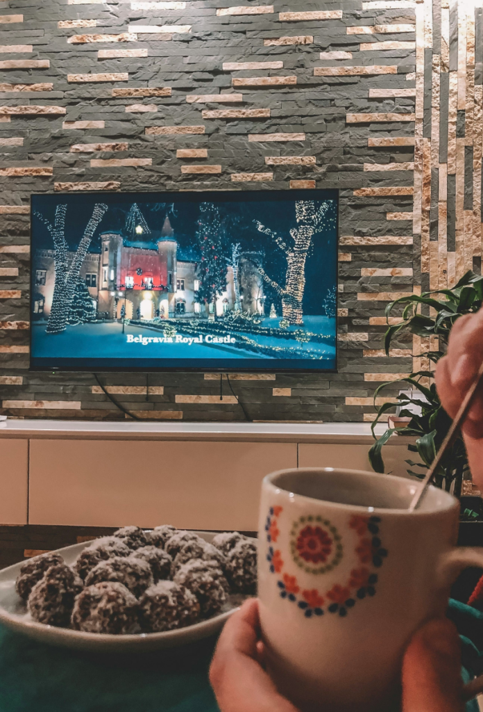 Karácsonyi film tévén, pohárban kanállal kevergeti az italát férfi, kókuszgolyók az asztalon