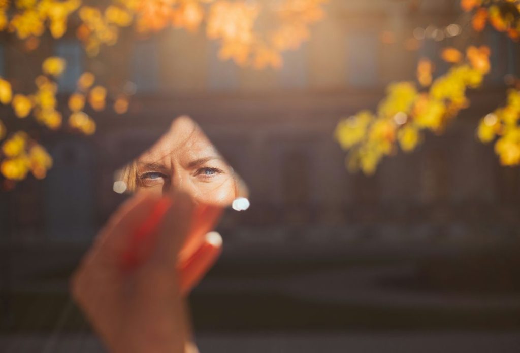 Nő őszi falevelek alatt tükördarabban nézi magát