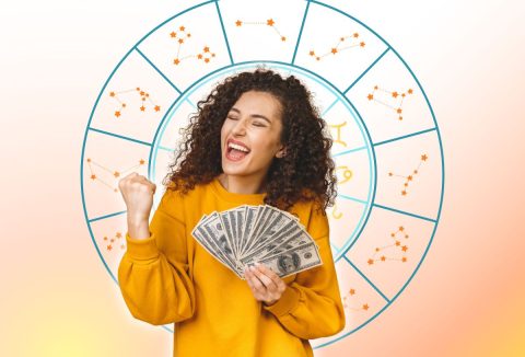 Egy barna hajú nő sok pénzt tart a kezében és örül. A háttérben a zodiákus csillagjegyeinek szimbóluma.