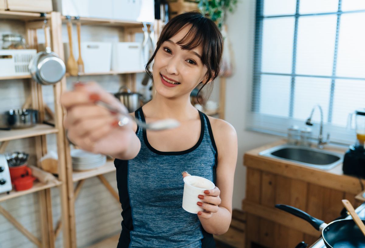 Fiatal ázsiai nő egy kanál joghurtot tart a kamera felé