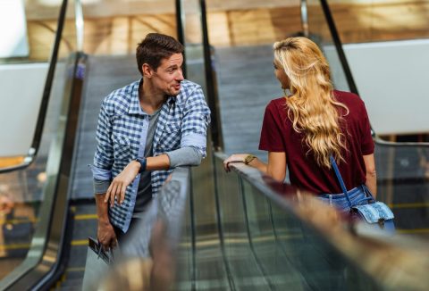 Barna hajú férfi és szőke hajú nő mozgólélpcsőn szembe megy és beszélget