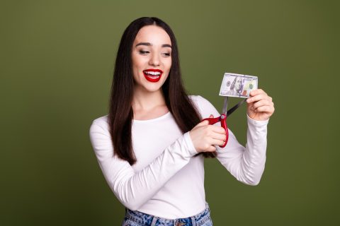 szép fiatal nő ollóval vág el egy papírpénzt
