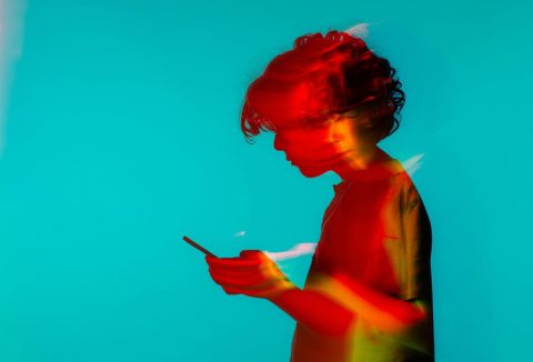 Számítógépes grafika, pirosas fényben elmosódott tinifiú telefonoz kék háttér előtt