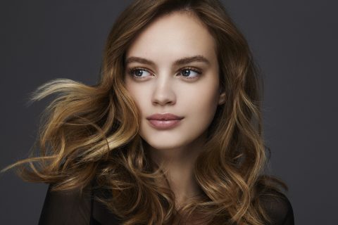 Szőkésbarna hajú nő oldalra néz és visszafogottan mosolyog