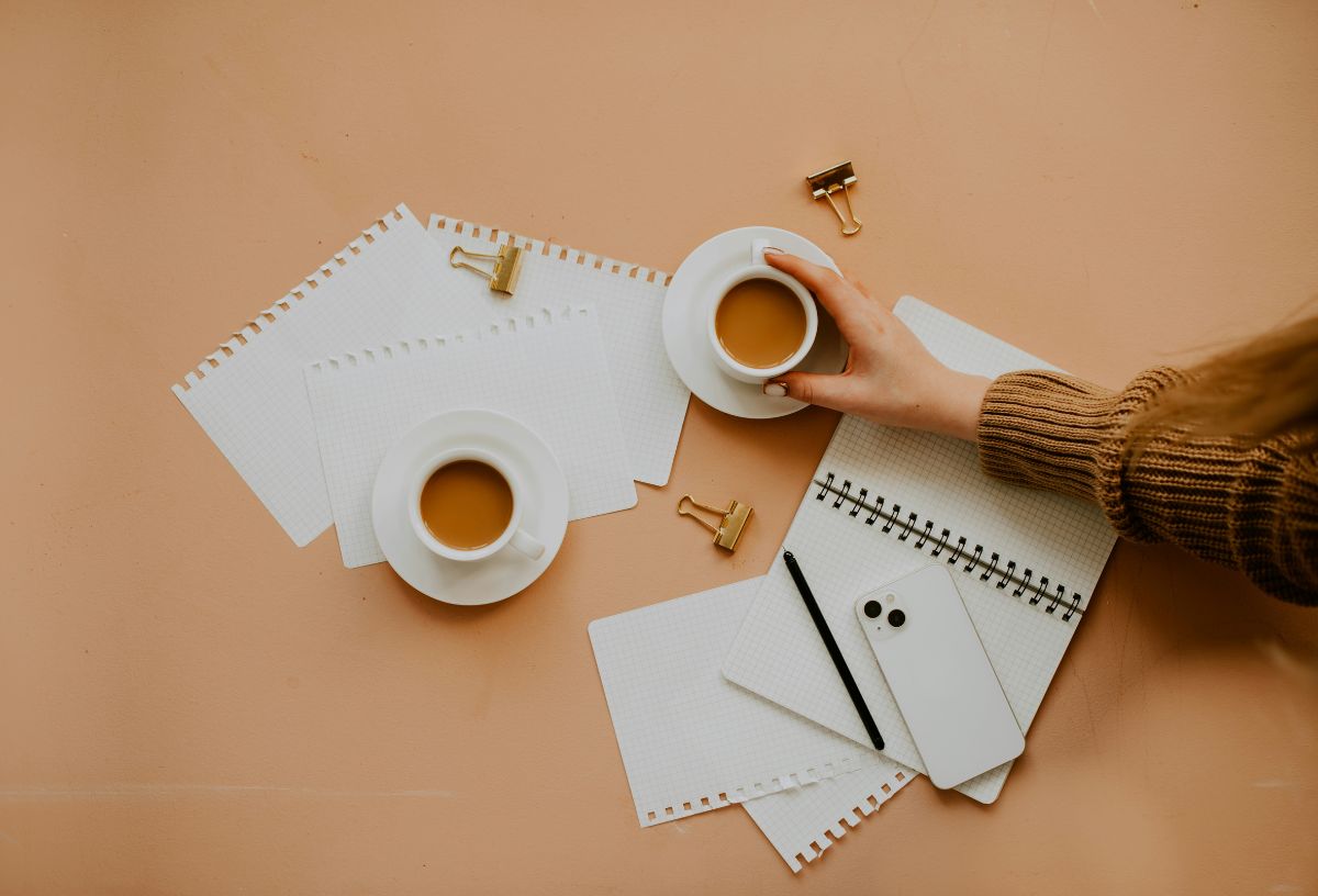 Karamell színű asztalon tervező, kitépett lapok, két csésze kávé és egy nő keze