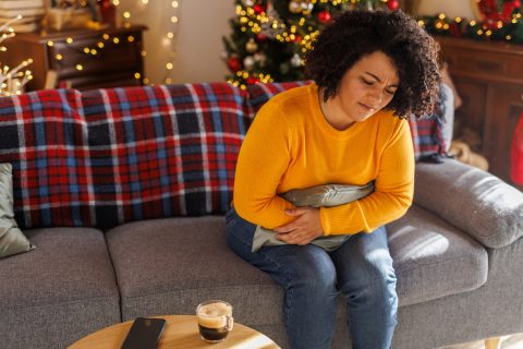 Egy fiatal nőről, aki a kanapén ül, egy párnát ölel, miközben fájdalmas görcsökkel küzd.