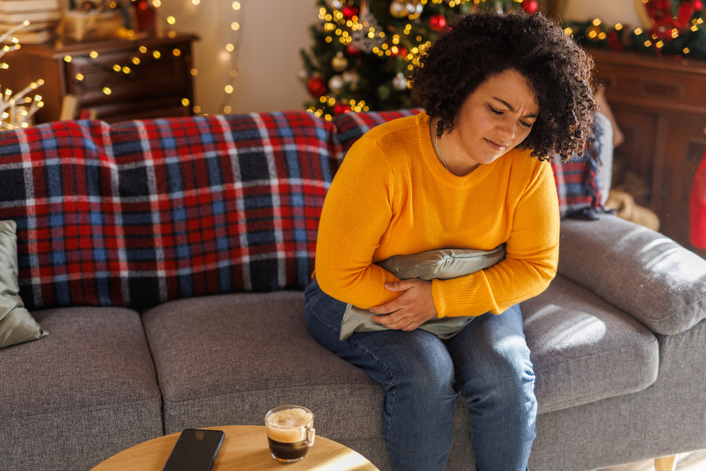 Egy fiatal nőről, aki a kanapén ül, egy párnát ölel, miközben fájdalmas görcsökkel küzd.