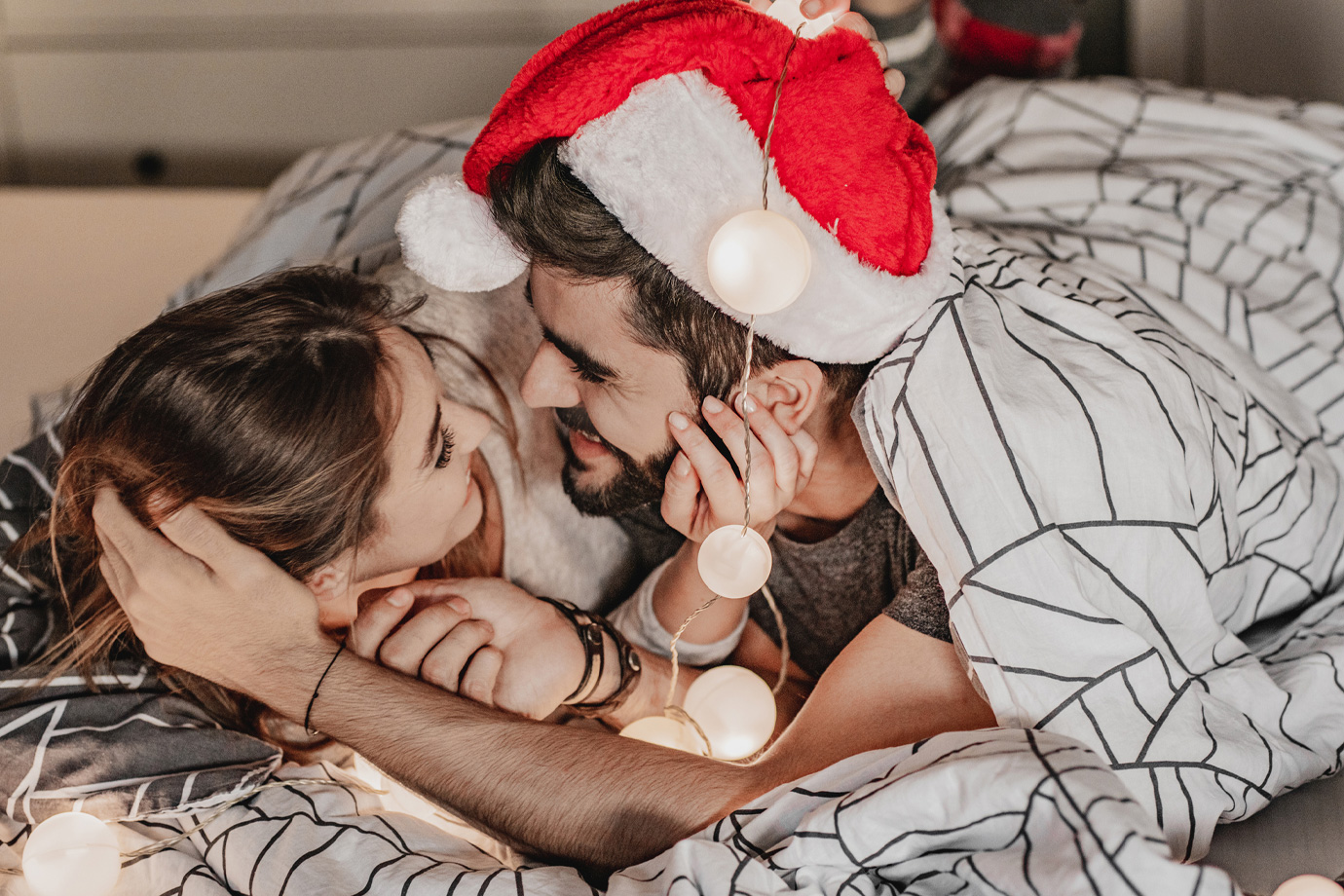 Egy nő és egy Mikulás sapkás férfi összebújva fekszenek az ágyban