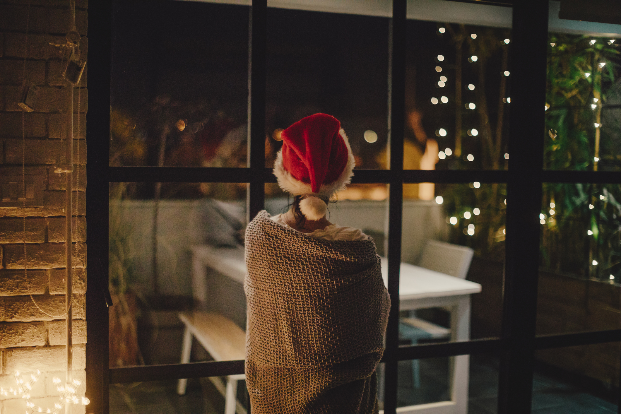 Fiatal nő, aki otthonában tölti a hangulatos karácsonyi estét, és kinéz az ablakon