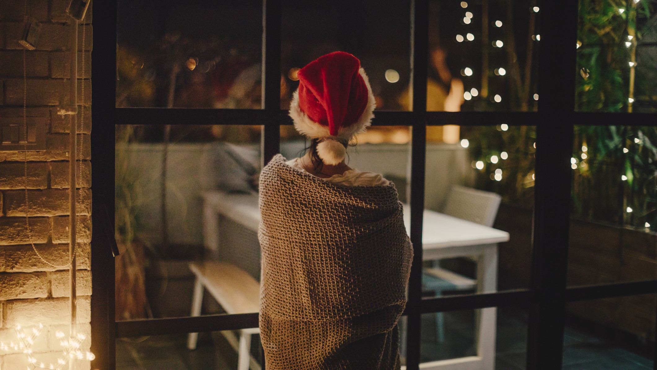 Fiatal nő, aki otthonában tölti a hangulatos karácsonyi estét, és kinéz az ablakon