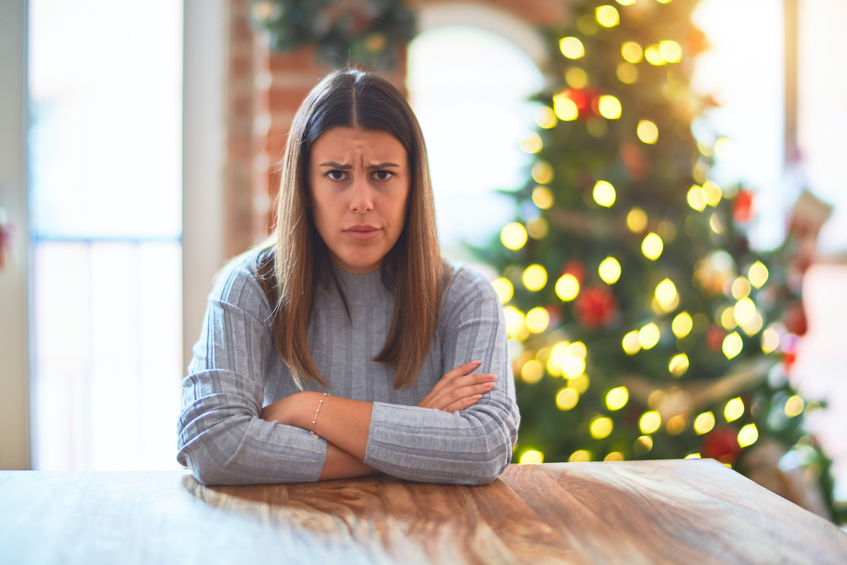 karacsony-2025-5-mondat-ami-tonkreteszi | Marie Claire boldogtalan, kérdő arckifejezéssel ül egy nő a karácsonyfa előtt az asztalnál