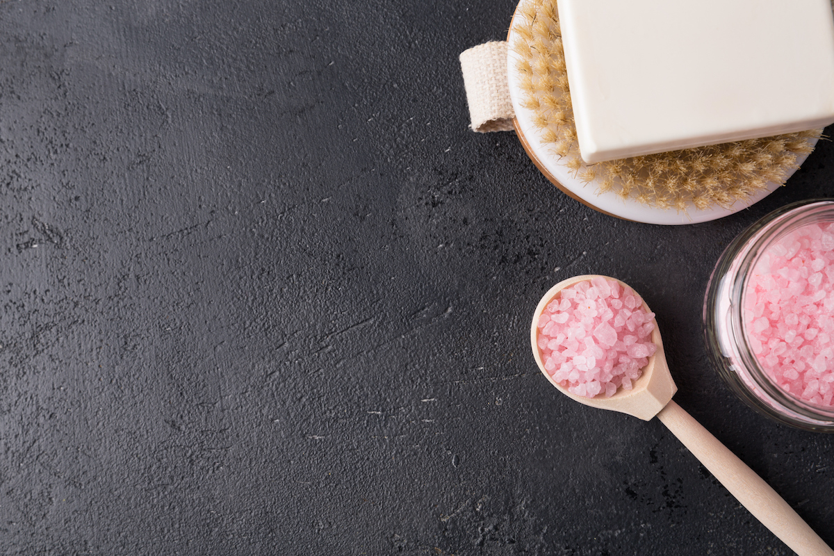 sos-furdo-igy-hasznald-a-spiritualis-erejet | Marie Claire sötét háttéren szappan, fürdőkefe és rózsaszín fürdősó