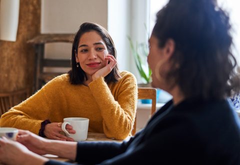 Két nő ül az asztalnál a konyhában és beszélget.
