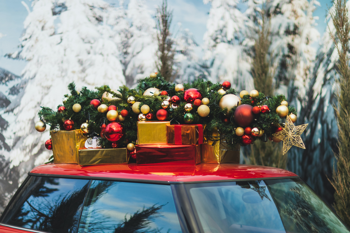 piros autó tetejére rögzített, feldíszített karácsonyfával és ajándékokkal