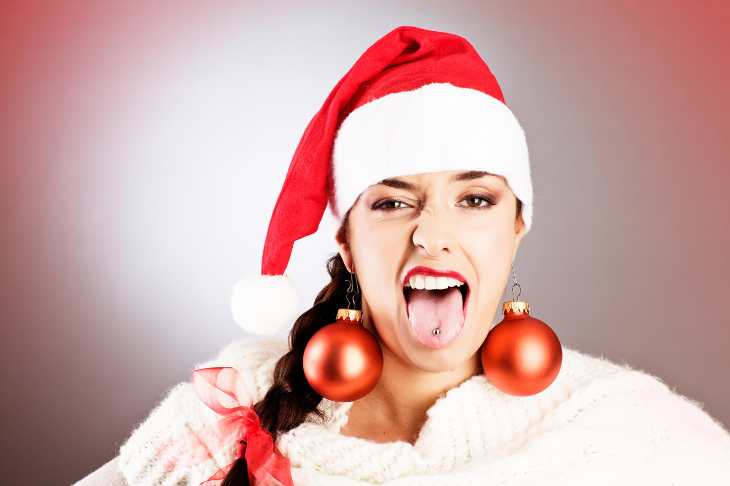 Egy nő, akinek elege van a karácsonyból, kinyújtja a nyelvét, karácsonyi díszeket visel fülbevalóként, és Mikulás sapkája van.