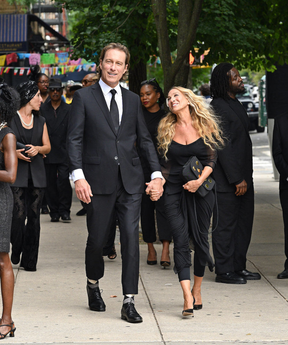 John Corbett fekete öltönyben és Sarah Jessica Parker fekete ruhában kézen fogva az utcán az És egyszer csak... forgatásán, 2024, New York City. 