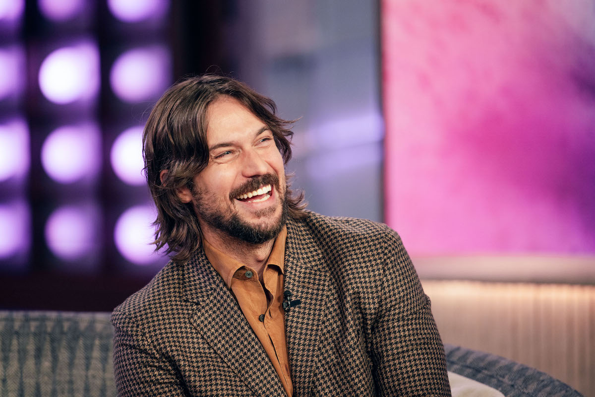 Lucas Bravo narancs ingben és kockás zakóban nevet