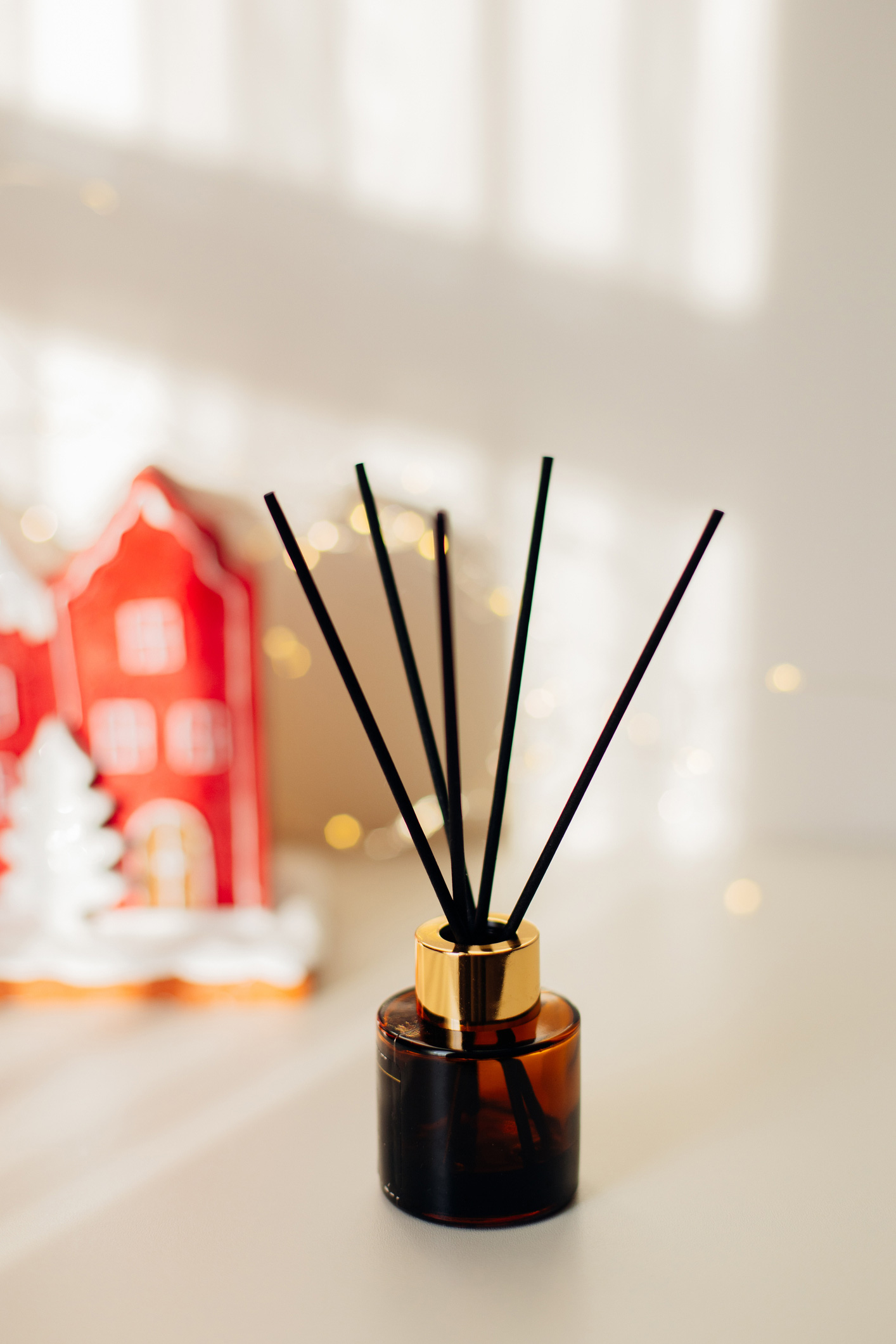 Fekete palack fekete fapálcákkal és piros karácsonyfadíszes kerámia házzal a háttérben