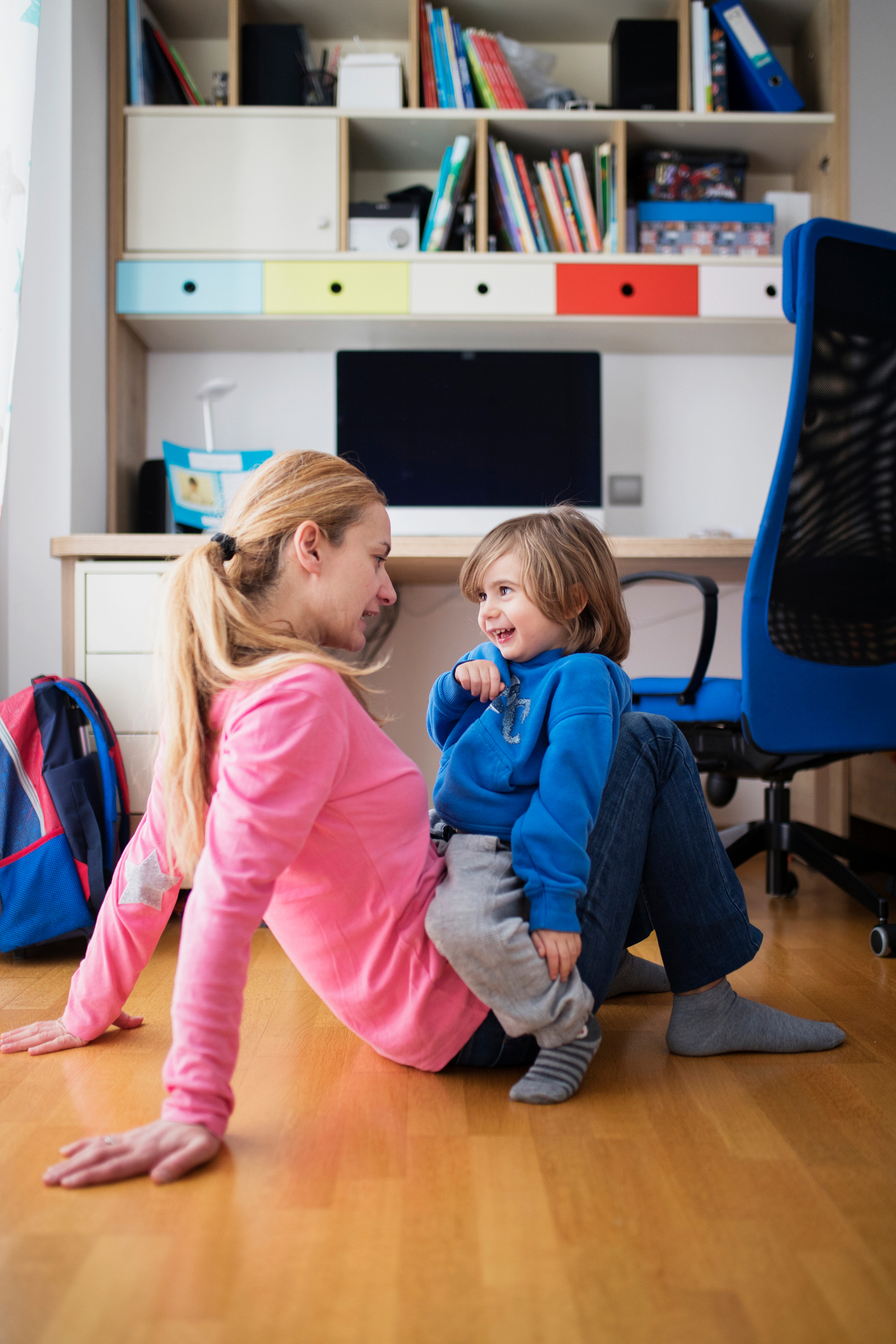 a-szoros-kotelekek-kialakitasanak-titka | Marie Claire Egy anya és kisgyermeke játékos pillanatokat töltenek együtt hangulatos szobájuk padlóján, könyvek és színes tárolók között, vidám légkört teremtve.