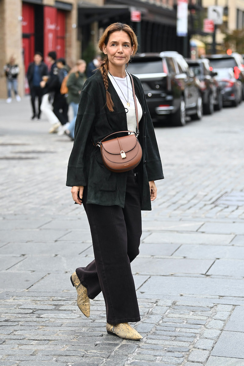 Katie Holmes 2025 októberében New Yorkban, DeMellier táskával, fekete nadrágkosztümben és befont hajjal.