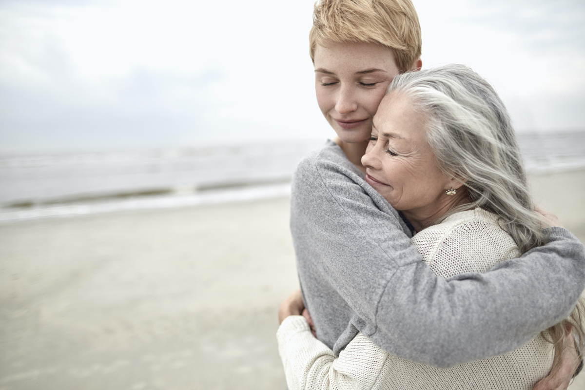 fiatalabb rövid hajú szőke nő átölel egy idősebb hosszú hajú nőt tengerparton