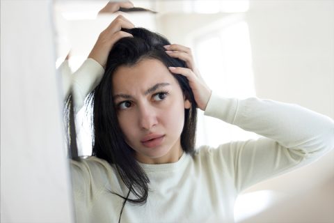 Egy nő hajproblémákkal küzd, és a tükör előtt nézi a haját