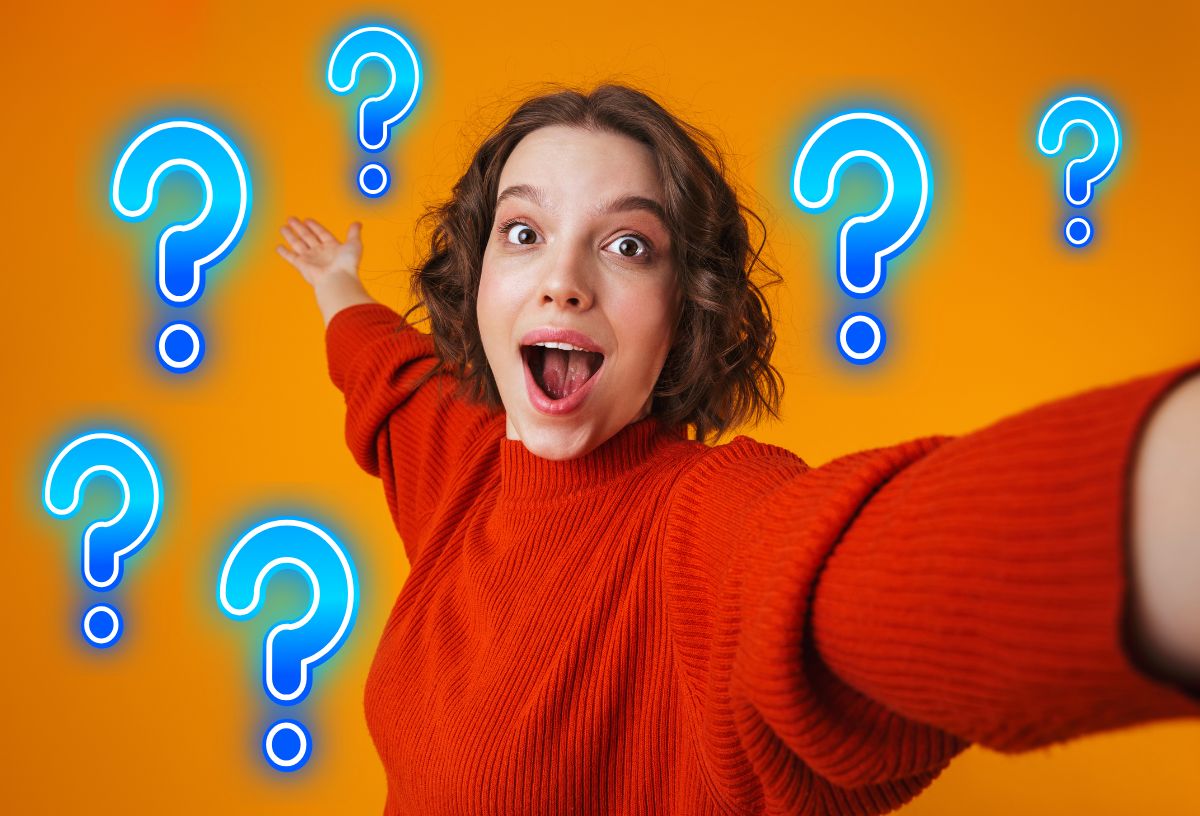 Fiatal, bob hajú nő piros pulcsiban csodálkozó arccal tárja szét a karjait félig oldalnézetben, narancsszínű háttér, kék kérdőjelek