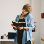 kék inges, szemüveges nő füzetet tart és telefonál