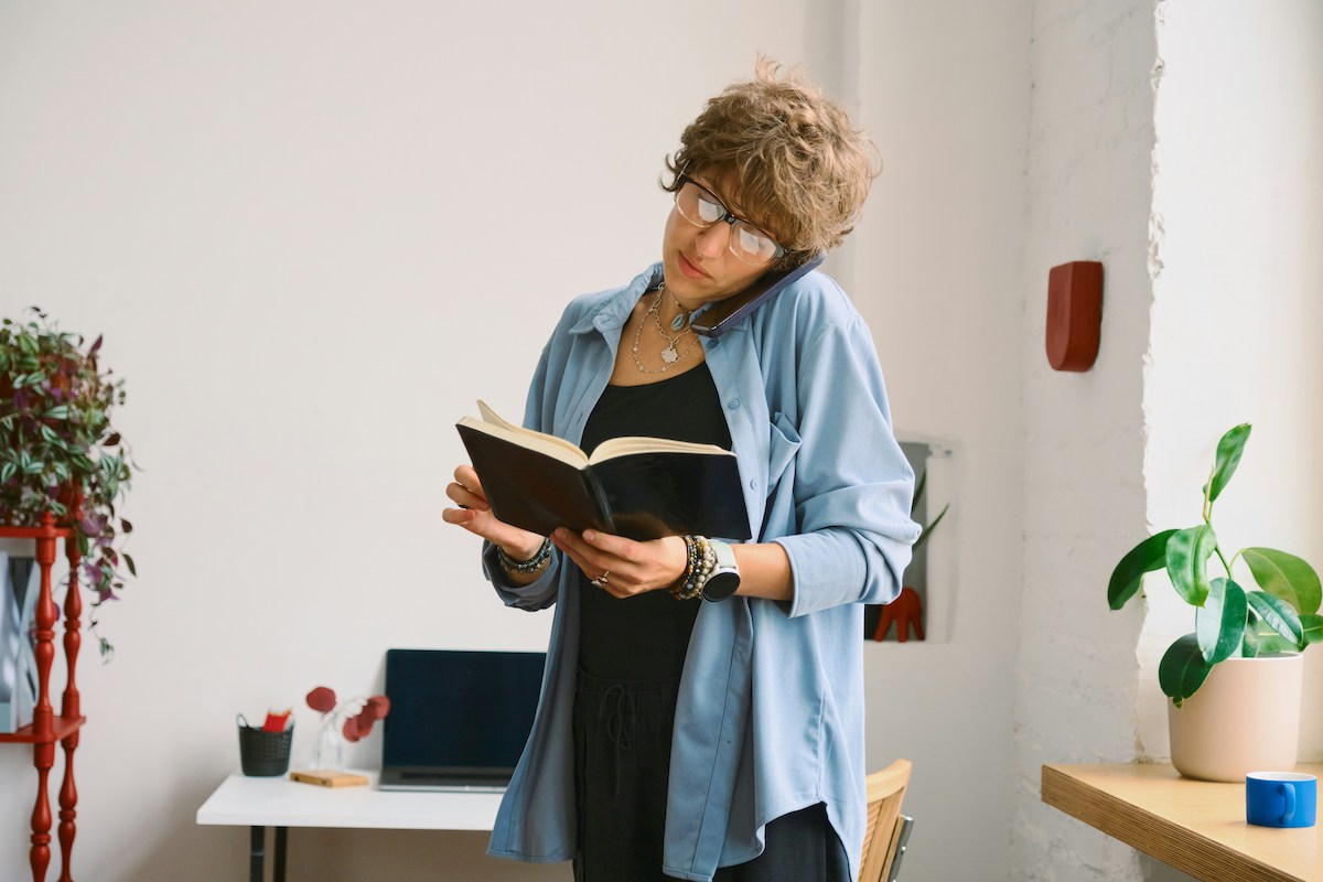 kék inges, szemüveges nő füzetet tart és telefonál