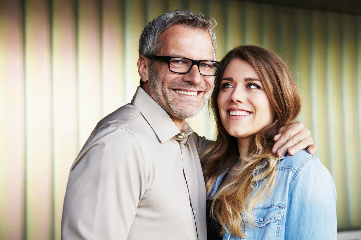 Idősebb szemüveges férfi egy fiatal nővel az oldalán, mindketten mosolyognak