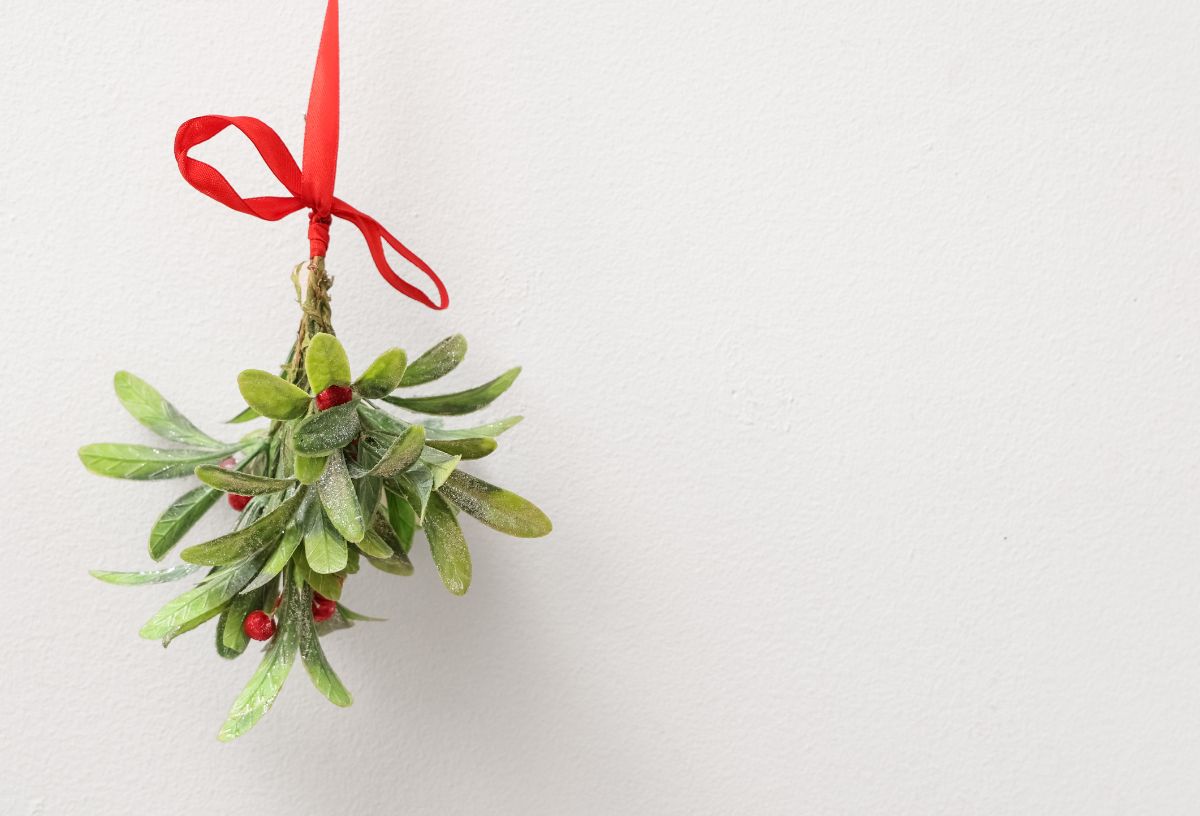 Piros szalagra felakasztott fagyöngy fehér fal előtt