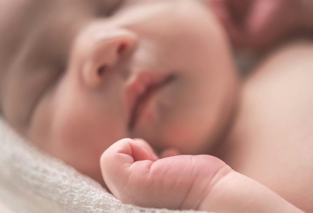 Alvó kisbaba közelről, fókuszban a keze behajlított ujjakkal
