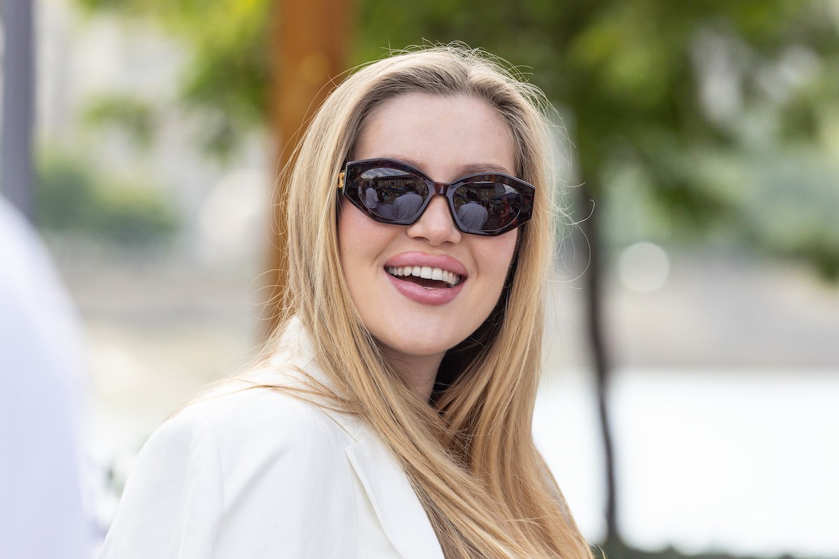 Buzsik Borka fehér felsőben és napszemüvegben, hosszú szőke hajjal