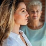 szőke nő az előtérben profilból, mosolyog, a háttérben elmosódottan idősebb nő