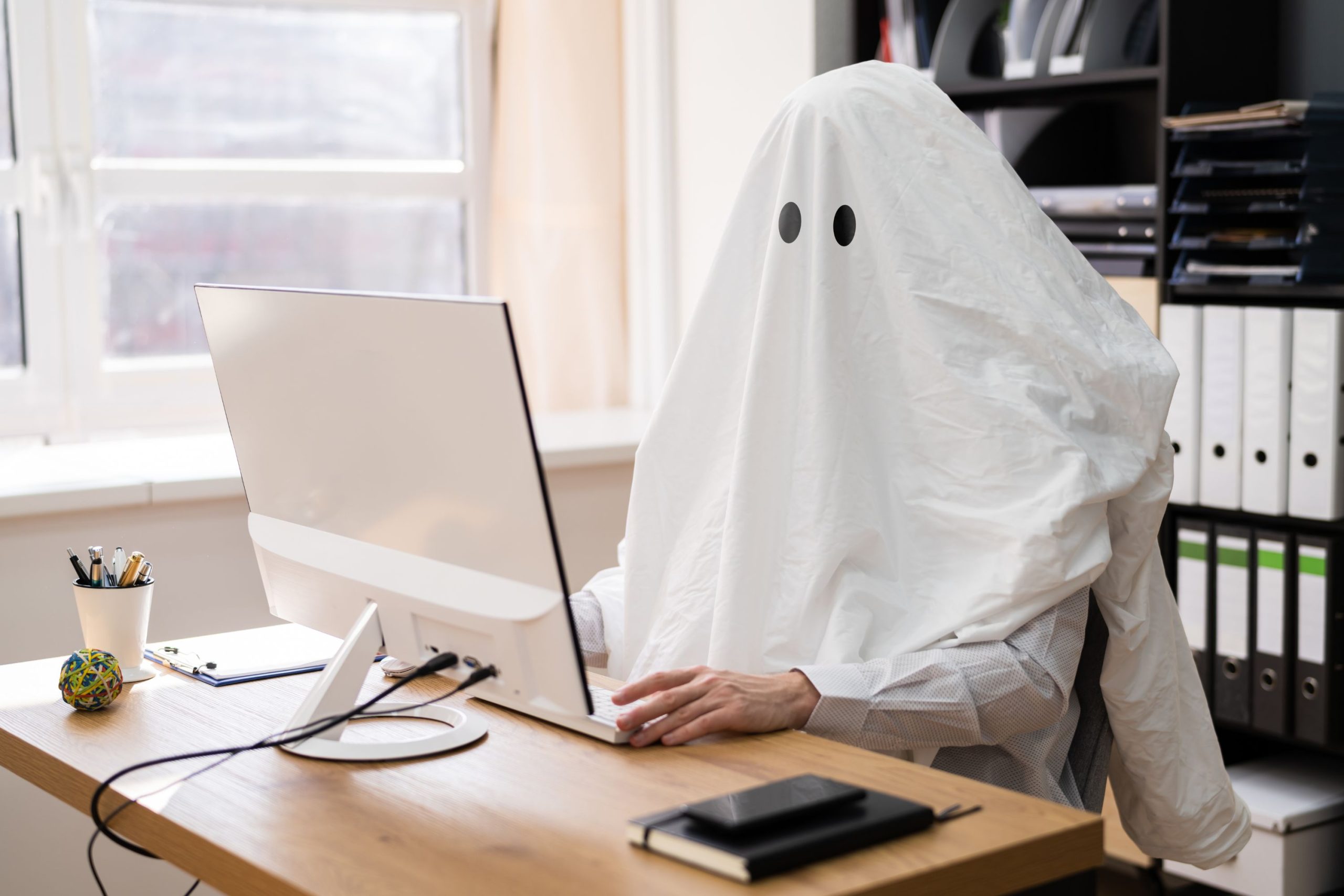 Szellemnek beöltözött alak ül a monitor előtt