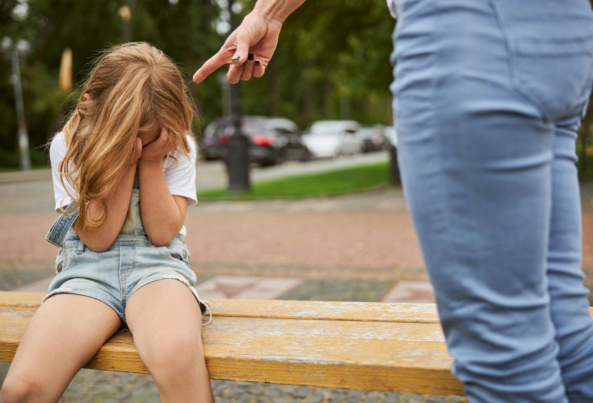 Szigorú anyuka fenyegetően mutat az ujjával a gyerekének, aki kezébe temeti az arcát padon ülve