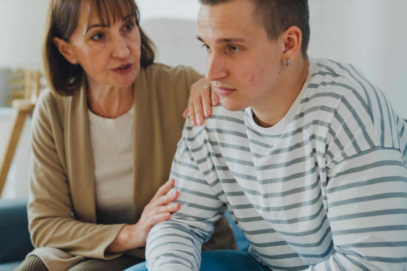 Anya vigasztalja tinédzser fiát egy nehéz érzelmi pillanatban a kanapén a nappaliban, otthon