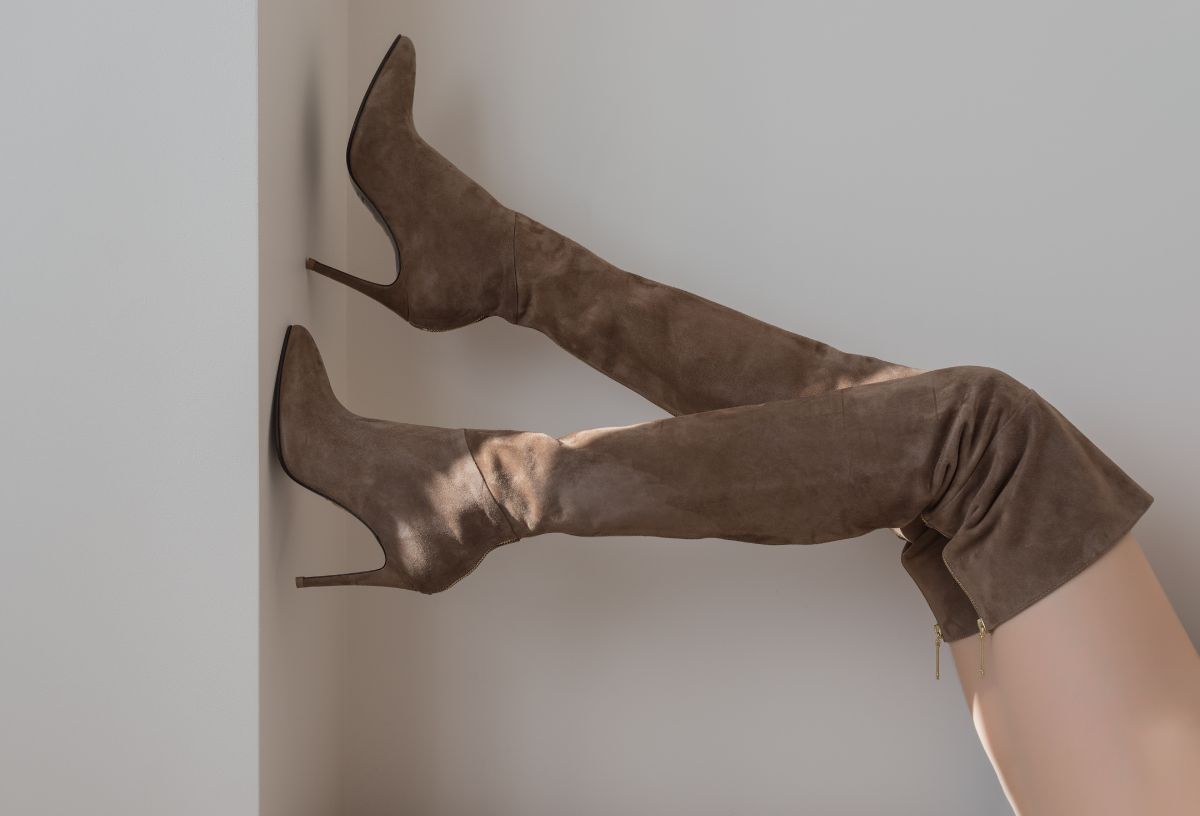 Női láb falnak támasztva drapp velúr magas sarkú combcsizmában