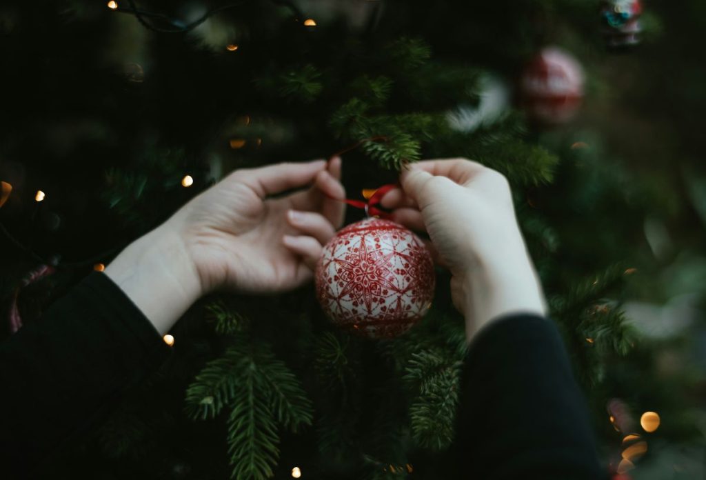 karacsonyfa-diszites-gomb-disz | Marie Claire Nő keze, amint nagyméretű piros-fehér mintás gömbdíszt akaszt a karácsonyfára