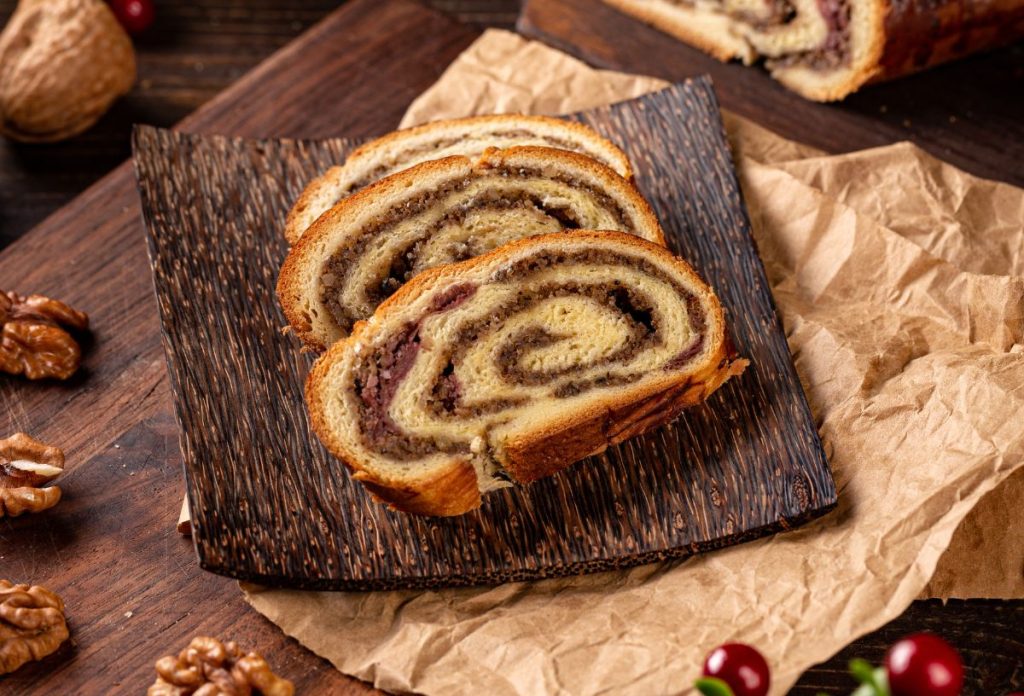 karacsonyi-menu-dios-bejgli-szaj-egeszsege | Marie Claire Diós bejlgi kókusztálon, alatta sütőpapír, mellette dió és piros bogyós növény dekorációnak