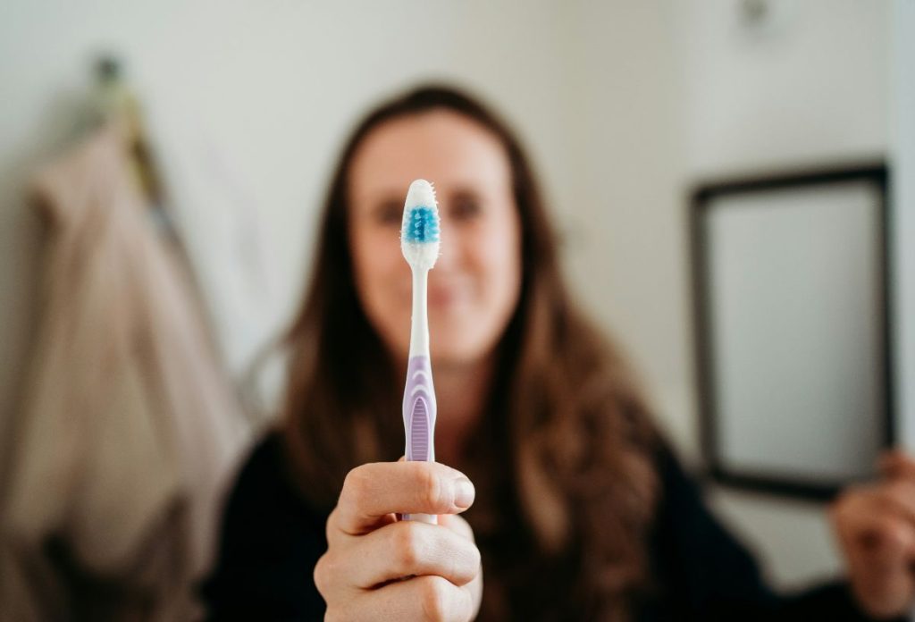 karacsonyi-szezon-fogmosas | Marie Claire Nő alakja elmosódva a háttérben, fókusz a fogkefét tartó kezén