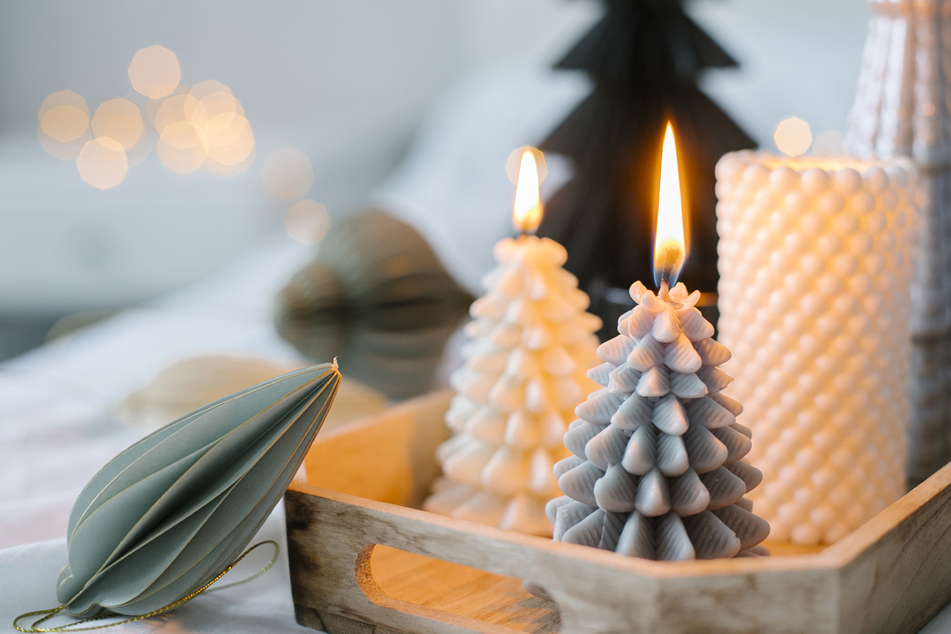 Hangulatos, fa alakú gyertyákkal és téli karácsonyi dekorációval díszített fa tálca fehér ágyon a hálószobában.